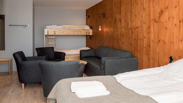 Une chambre moderne avec un lit superposé, deux canapés gris, une petite table et un mur en bois.