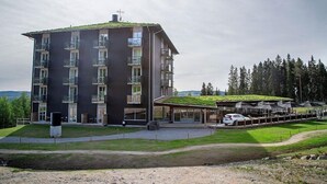 Un hôtel à plusieurs étages, doté de balcons, d’un espace extérieur couvert et d’une voiture garée devant.