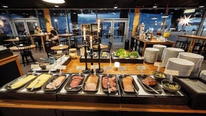 Un espace buffet proposant une variété de plats et offrant une vue sur le paysage urbain grâce à de grandes fenêtres.