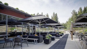 Un espace extérieur aménagé avec des tables et des chaises, protégé par de grands parasols, et une terrasse en bois.