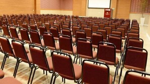 Un salón de conferencias con hileras de sillas rojas, una pizarra y una pantalla de proyector.
