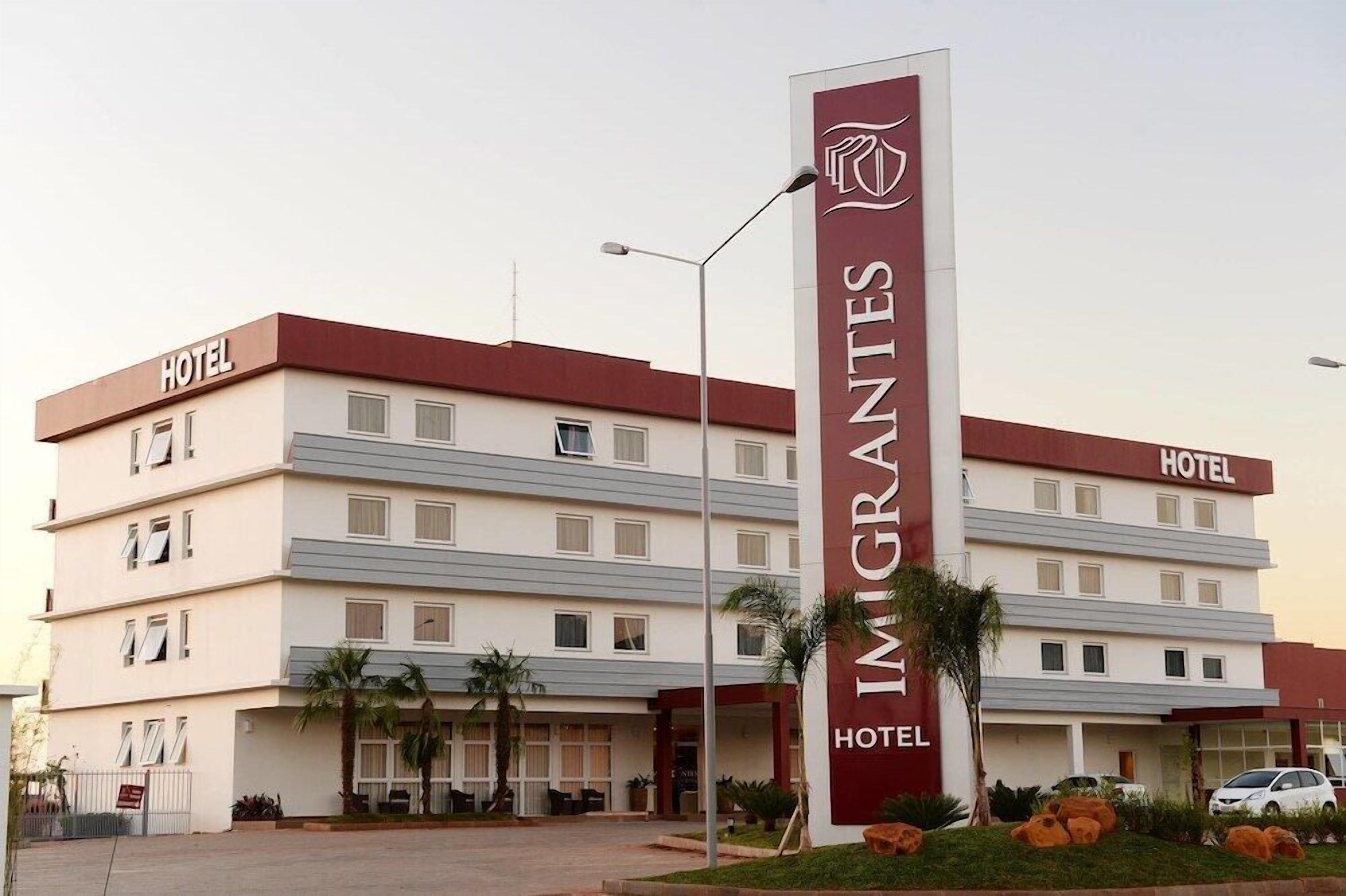 Un edificio de hotel de varios pisos con un llamativo letrero vertical que dice "IMIGRANTES HOTEL".