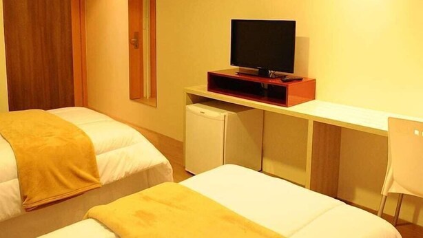 Una habitación de hotel con dos camas, un televisor sobre un mueble bajo, un refrigerador pequeño y un escritorio.