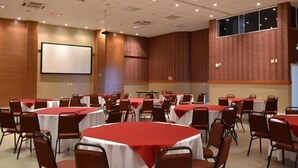 Un salón de conferencias con varias mesas redondas, cada una cubierta con un mantel rojo y rodeada de sillas marrones.