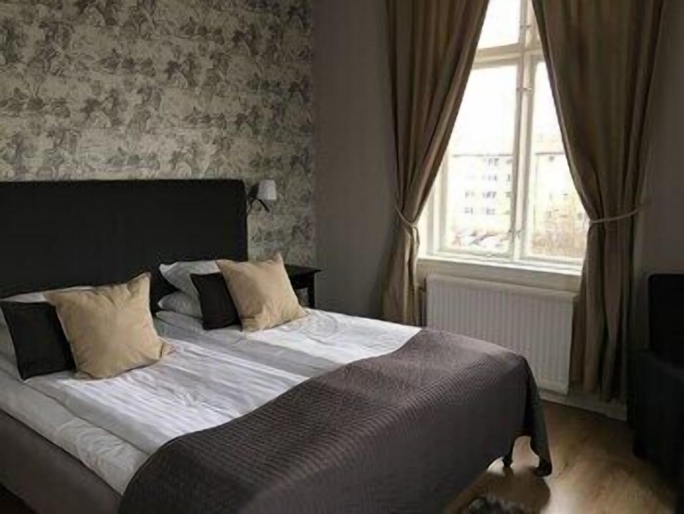 A bedroom with a large bed, a headboard, a nightstand, and a window with curtains.