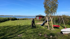 A grassy area with a swing set, a small red building, and a tree. - Apartment 1 with 2 bedrooms (4 adults + infant) on the ground floor - Villa Seeheim Ferienobjekt direkt (Boiensdorf)