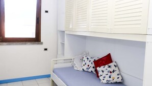 Een kleine kamer met een enkel bed en raam, met witte wanden en blauwe accenten.