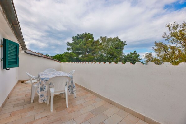 A small outdoor patio with a table and chairs, a white wall, and a view of trees and sky. - Cotoncello in a panoramic position (Marciana)