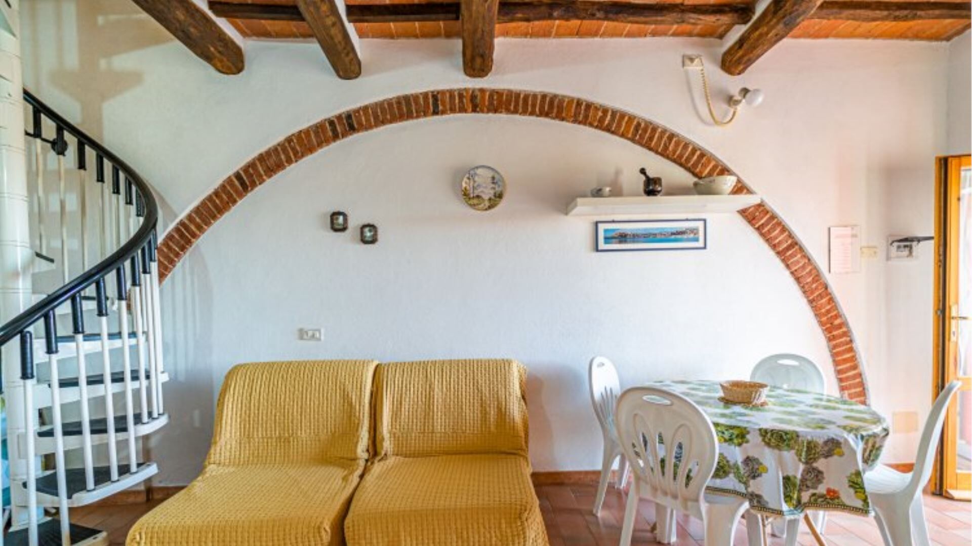 A cozy living area with a yellow sofa, a dining table with chairs, and a staircase.