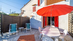 Een terras met een tafel, stoelen, een rode parasol en een houten hek.