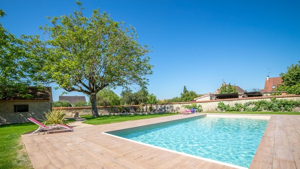 A rectangular swimming pool with a wooden deck, surrounded by a stone wall and greenery. - 50 Nuances de Bourgogne (Bligny-lès-Beaune)