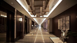 A long, well-lit hallway with a modern ceiling design, a decorative wall with artwork, and a statue of a bird on the right.