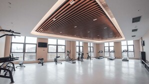A spacious gym with various exercise equipment, large windows, and a modern ceiling design.