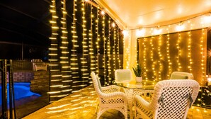 Eine Terrasse im Freien mit Korbstühlen und einem Glastisch, umgeben von Lichterketten.