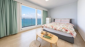 Une chambre à coucher avec un lit, une table de chevet avec une lampe, une fenêtre donnant sur la mer et une petite table avec une tasse et des biscuits.
