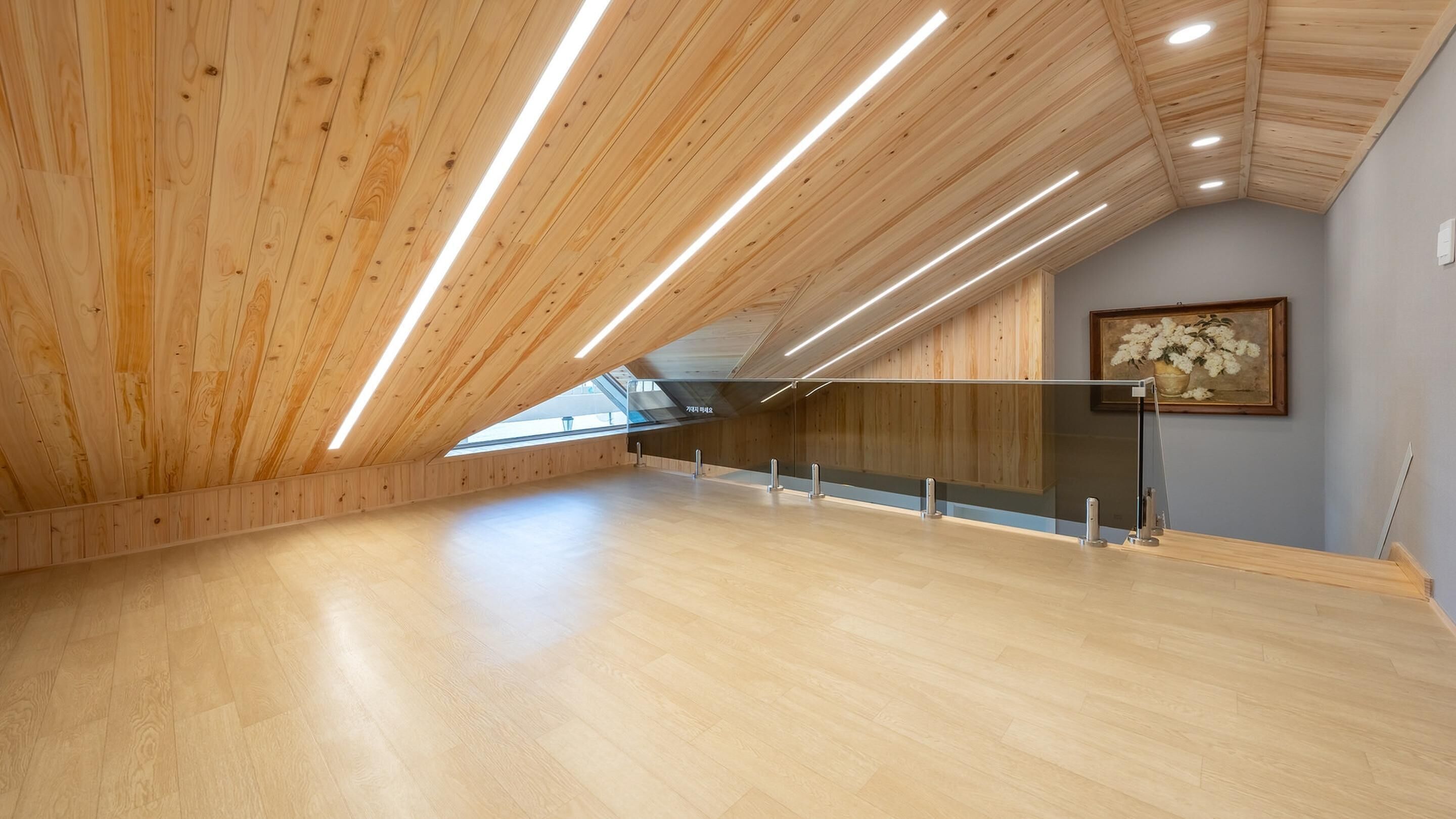 A spacious attic room with wooden slats on the ceiling and a large skylight.