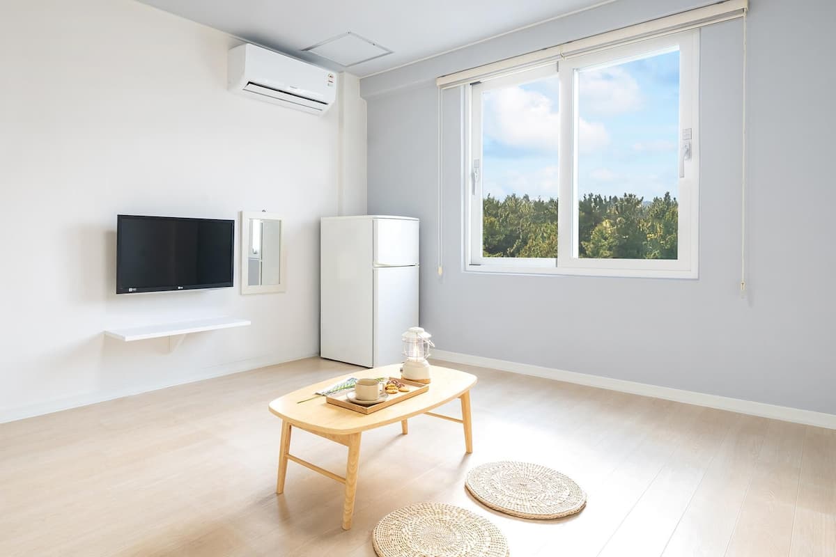 Een moderne, minimalistische woonkamer met een flatscreen-televisie, een witte koelkast en een houten tafel met een schaal lekkernijen.