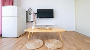 Een kamer met een houten tafel, een witte koelkast, een aan de muur bevestigde televisie en een decoratieve vogelkooi.