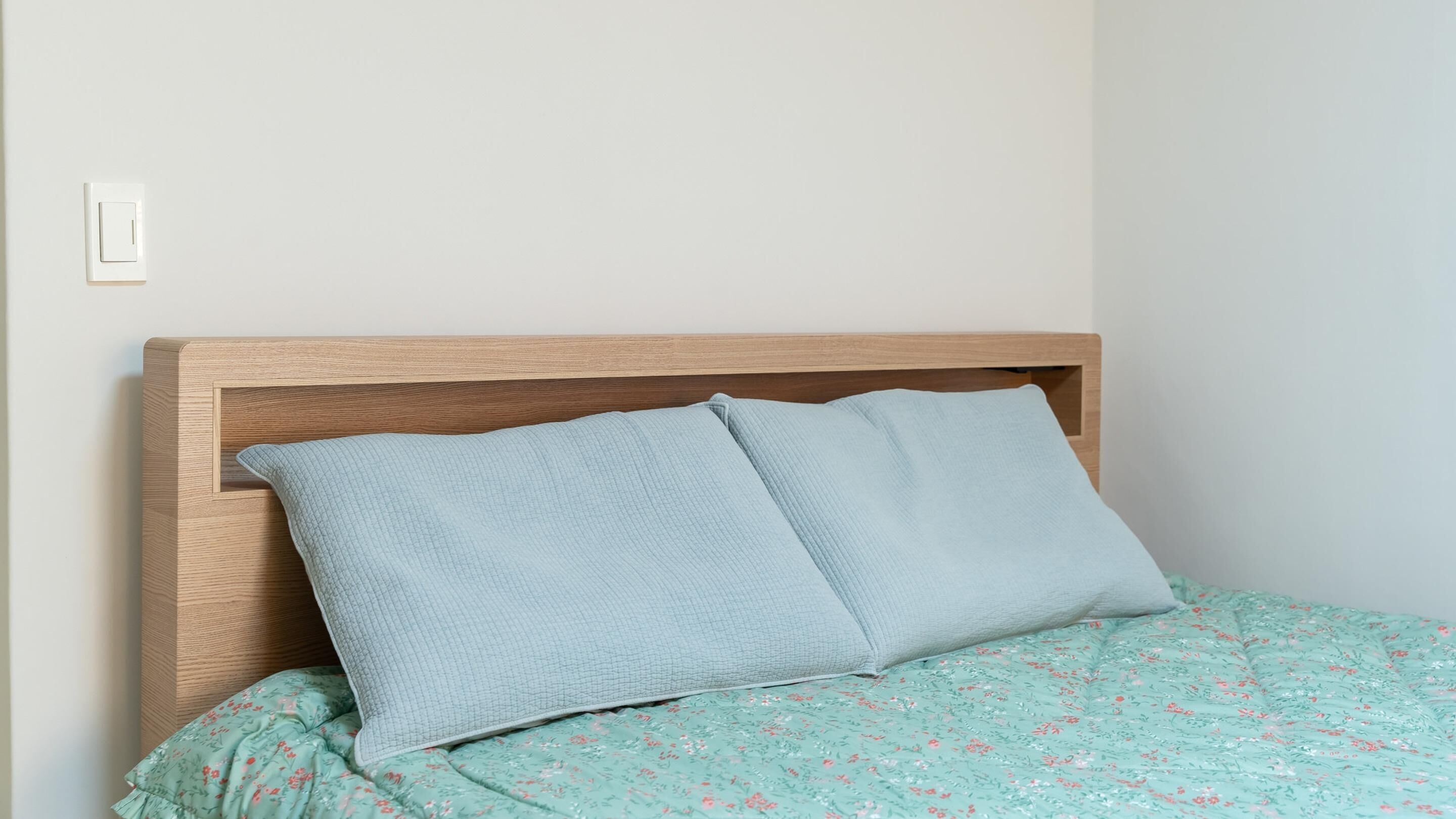 Una cama con cabecera de madera, colcha estampada con motivos florales y dos almohadas.