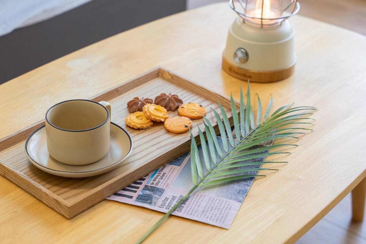 Een houten tafel met een kopje en schotel, koekjes, een kaars en een krant.