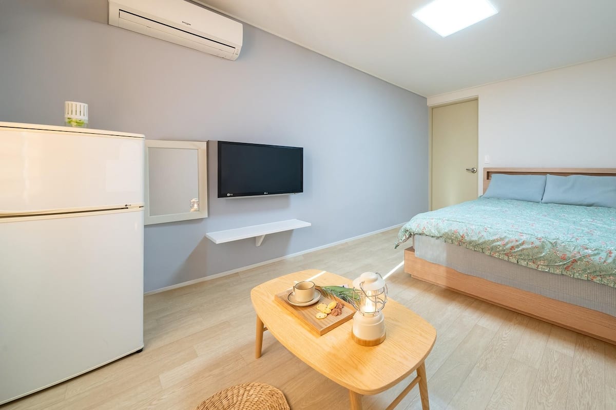 Een compacte kamer met een bed, een klein tafeltje met een lamp, een televisie en een koelkast.