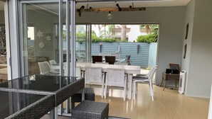 A modern patio with glass doors, wicker furniture, and a dining area with a table and chairs. - Entertainers Home at the Beach (Waihi Beach)