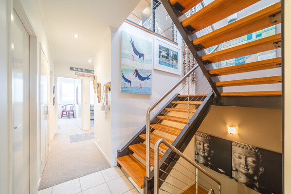 A modern interior with a staircase, wooden steps, metal railings, and artwork on the walls.