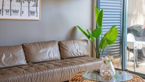 Een moderne woonkamer met een leren bank, een glazen salontafel en een groot raam met zonwering.