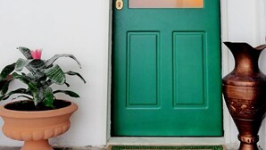 A green door with a frosted glass panel, a potted plant, a doormat, and a vase on the floor. - Palazzo Toraldo di Francia (Tropea)