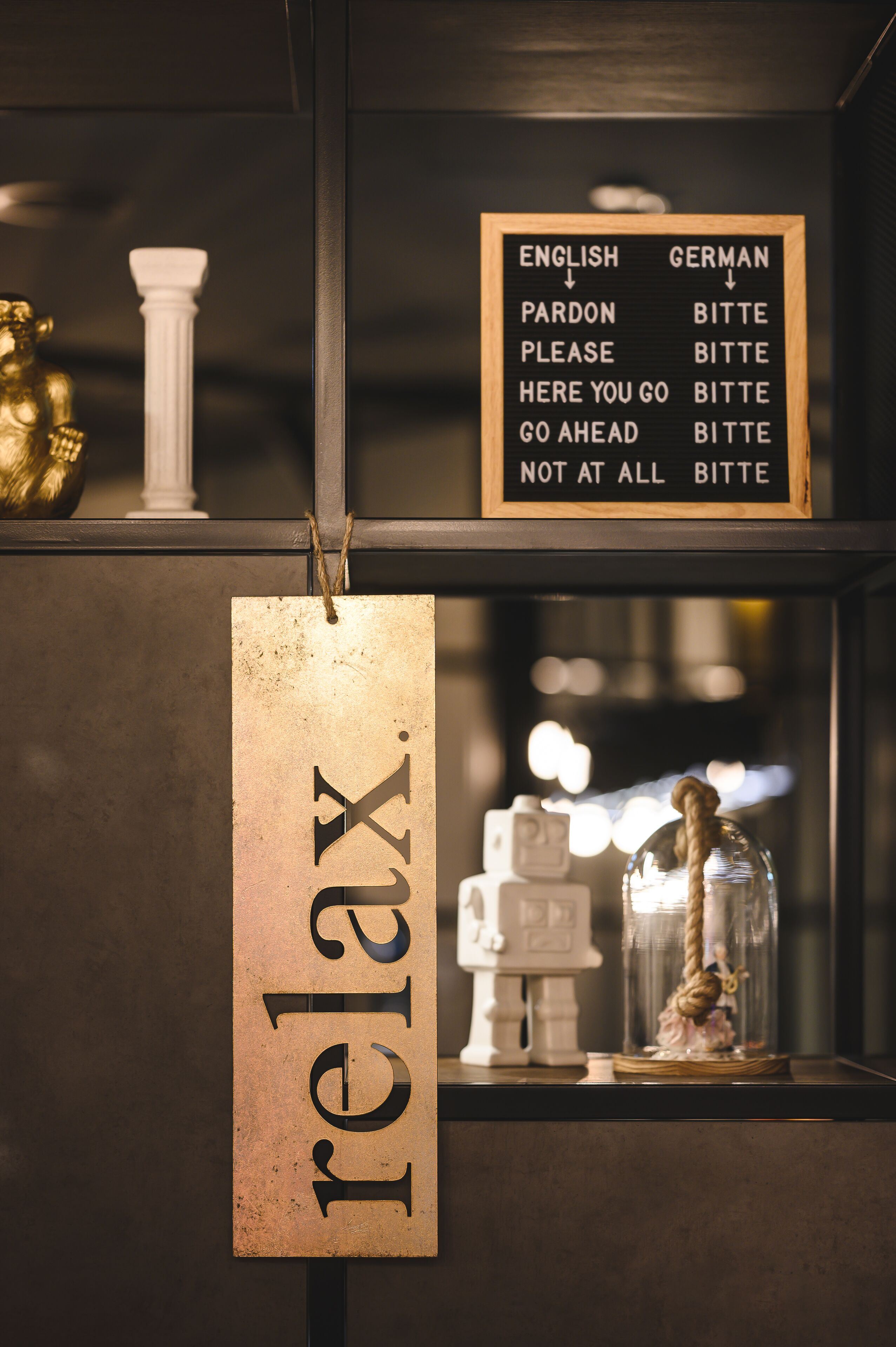 A sign with English and German translations of common phrases, a wooden sign with the word "relax.", and a glass dome with a figure inside.