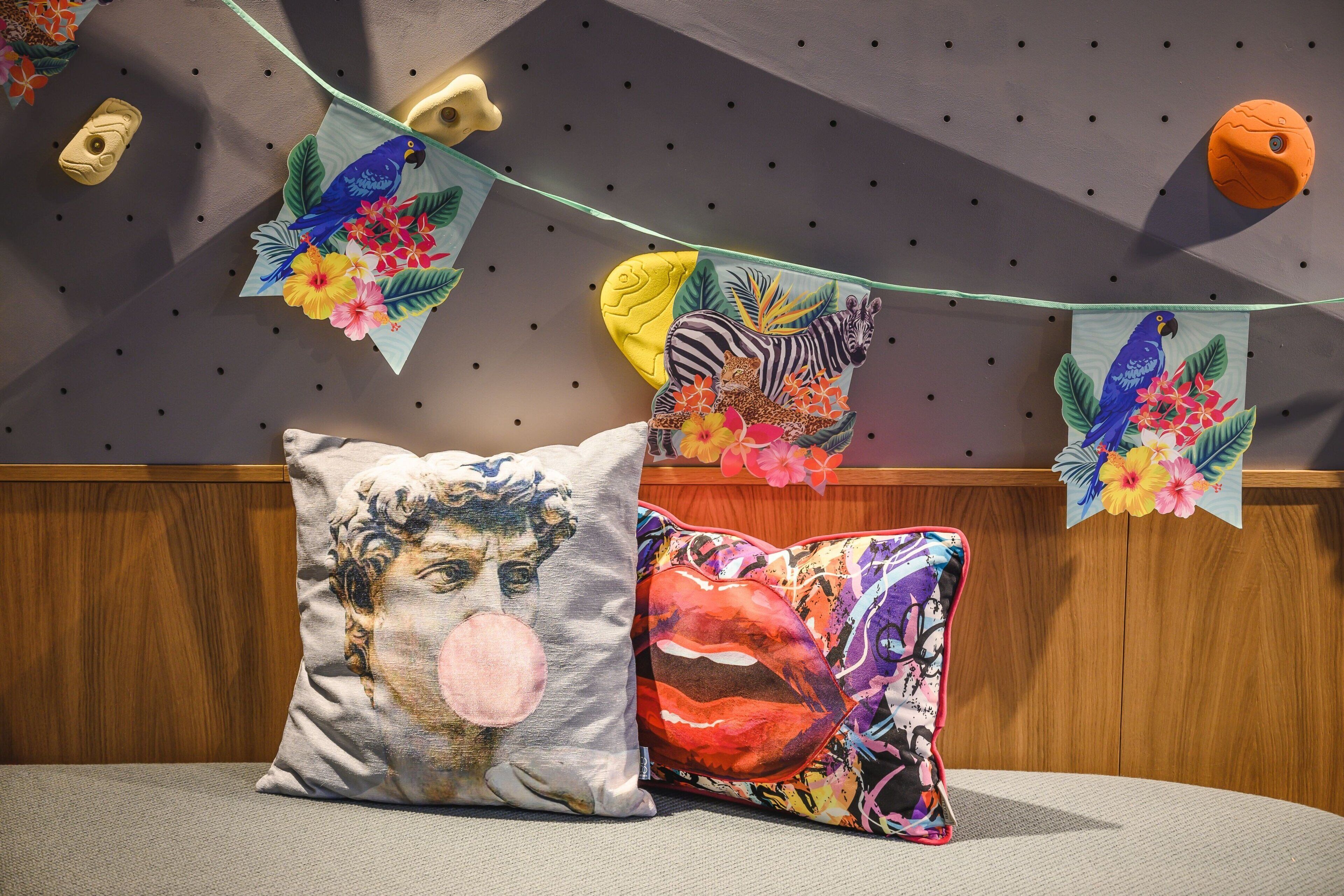 Ein Zimmer mit einer hölzernen Bank, zwei Kissen mit künstlerischen Motiven sowie einer Wand, die mit Anhängern und einer Lichterkette verziert ist.