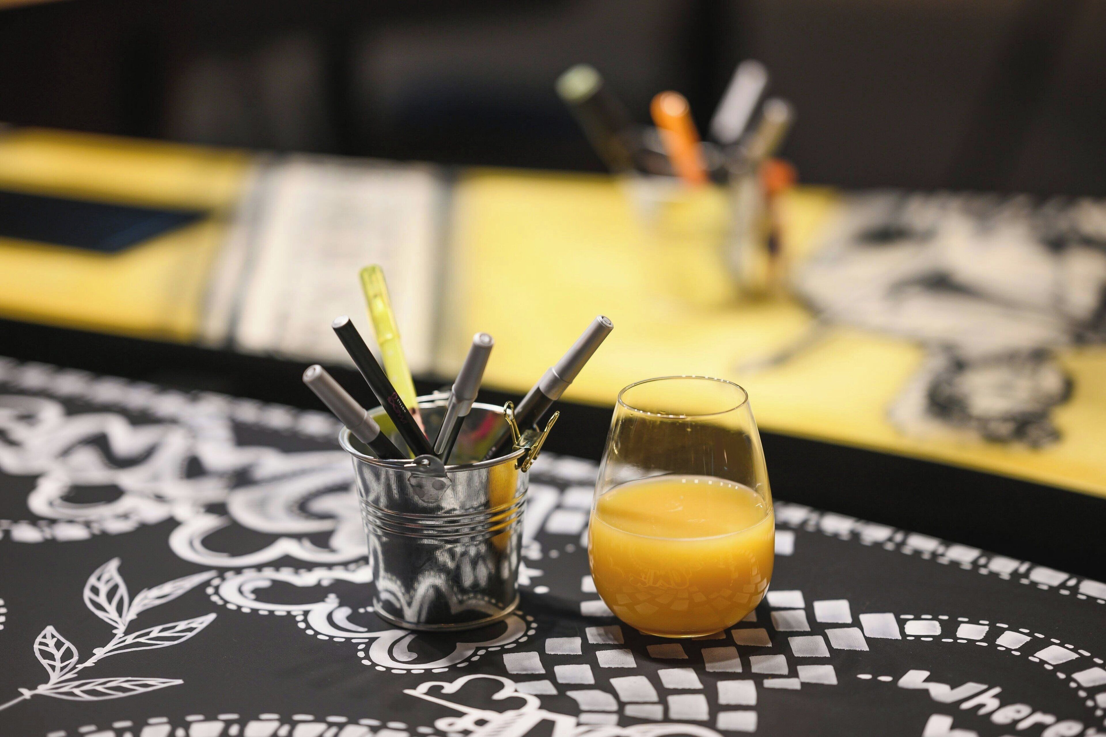 Une table avec un verre de jus d’orange et une tasse contenant des stylos.