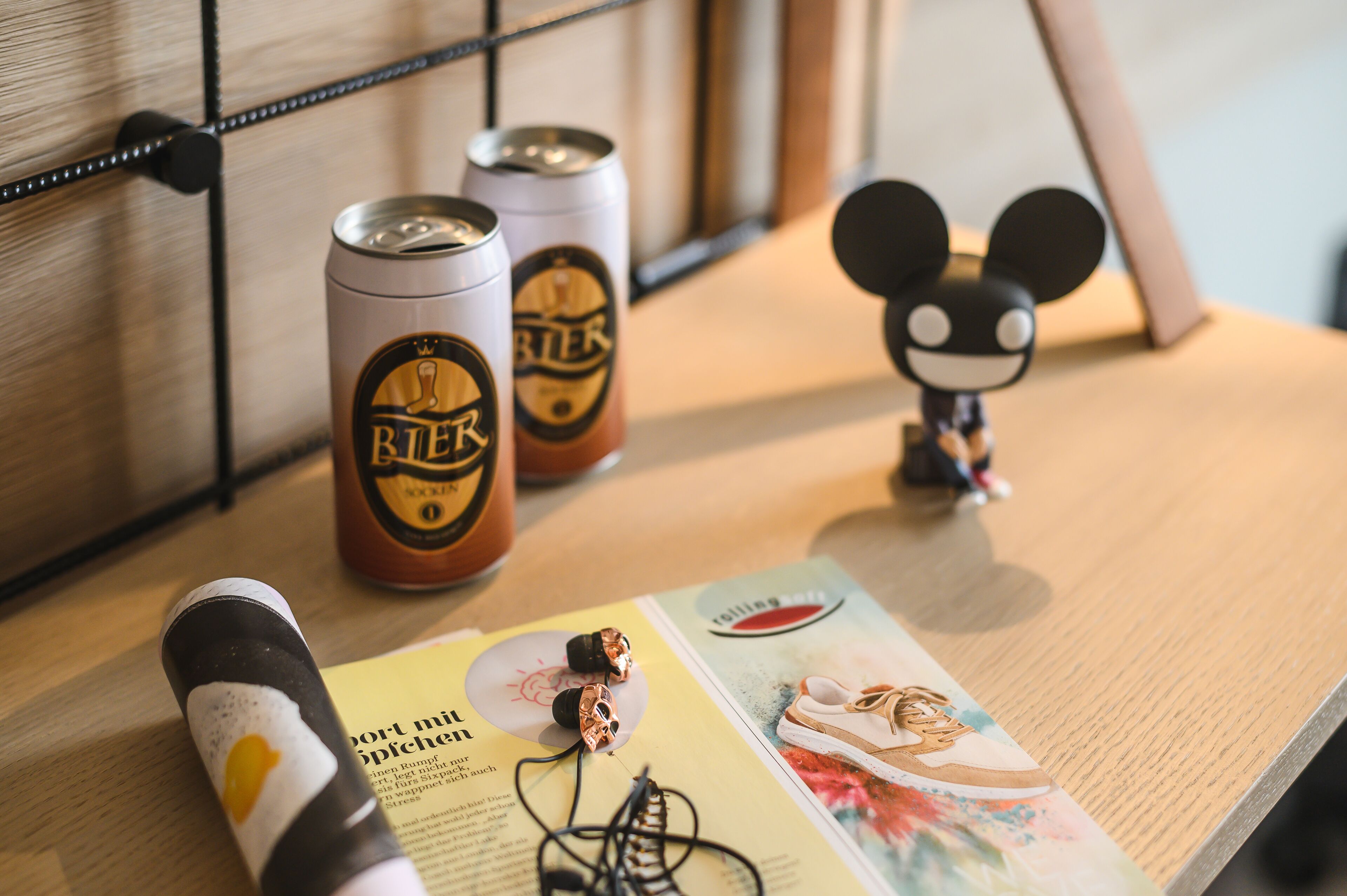 Ein Holztisch mit zwei Bierdosen, Kopfhörern und einer Mickey Mouse Figur.