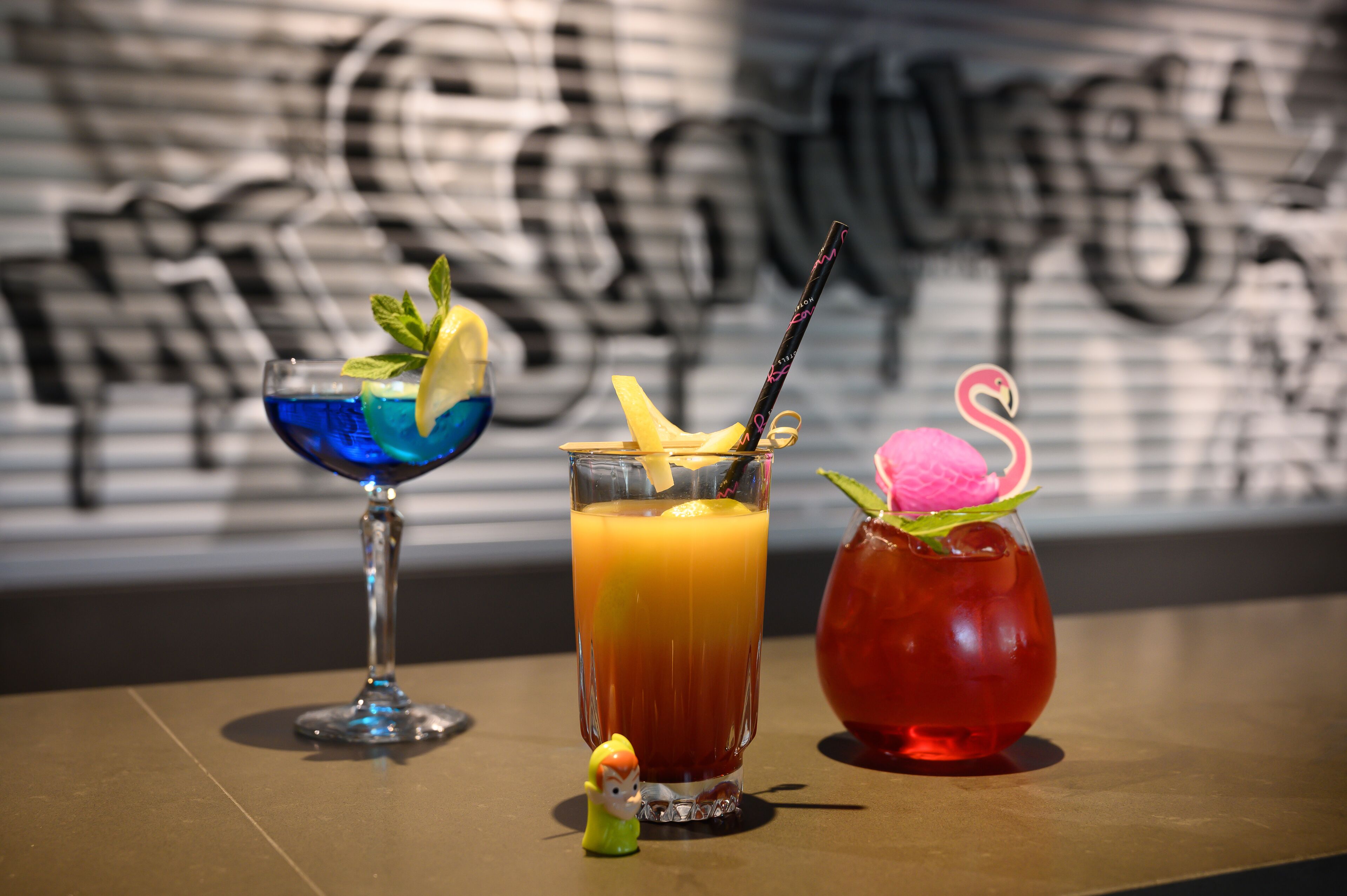 Three drinks on a table with a graffiti wall in the background.