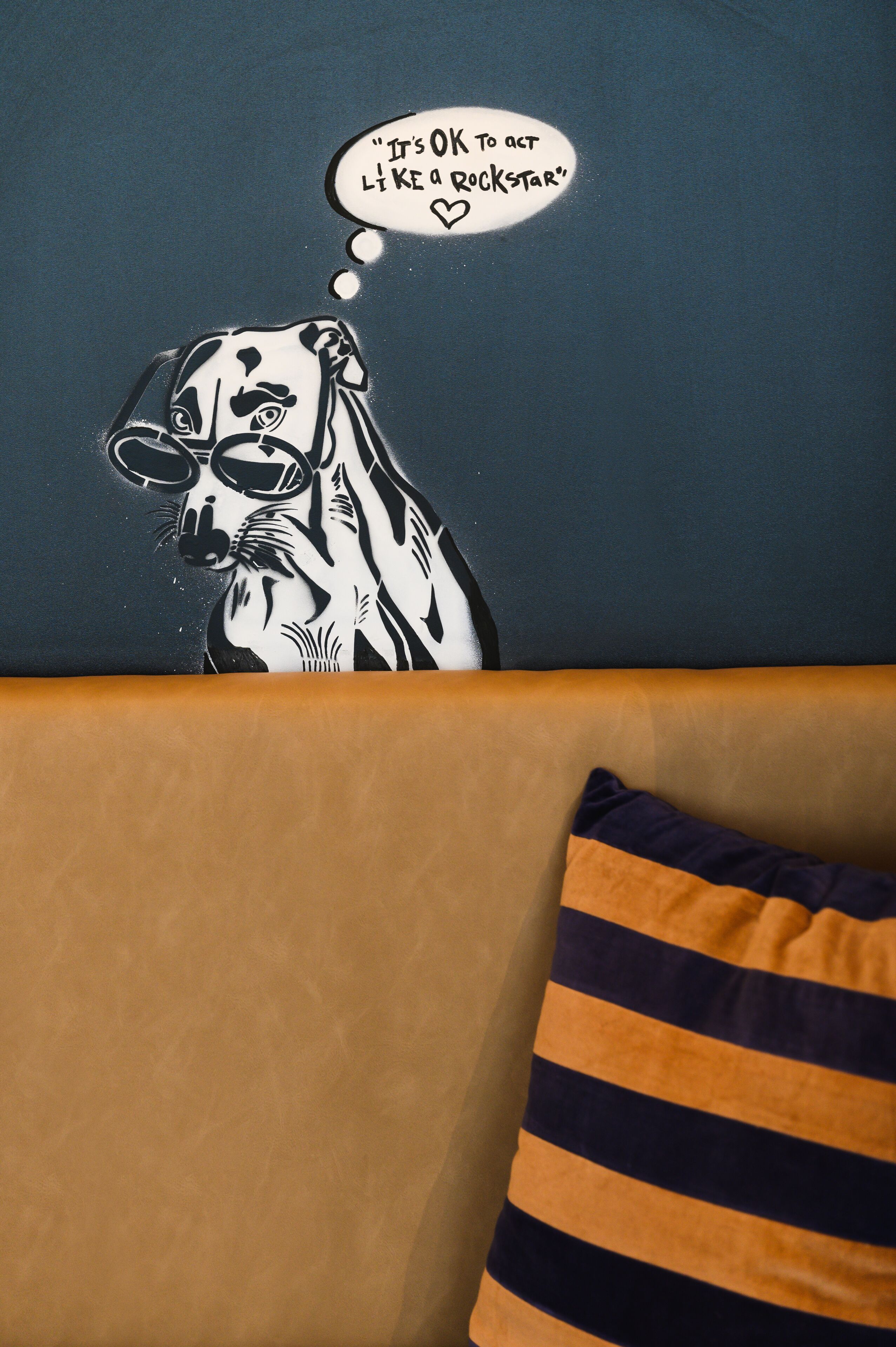 A wall with a black and white mural of a dog with sunglasses and a speech bubble saying "It's OK to act like a rockstar".