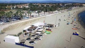 Een strandgebied met een rij strandstoelen en parasols, een klein gebouw met een plat dak en verschillende boten.