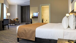 Et hotelværelse med en seng, et skrivebord, en stol, et fjernsyn og en dør til badeværelset.