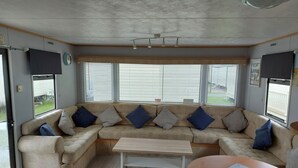 A cozy living area with a beige sectional sofa, a wooden coffee table, and a round table with a marble top. - Above & Beyond Caravans4hire Lyons Robin Hood Rhyl (Rhyl)