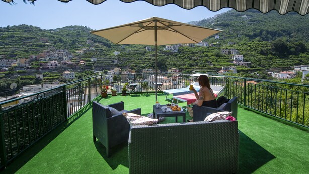 A terrace with outdoor furniture and a table, overlooking a hillside with buildings. - Sapphire house amalfi coast sea view (Minori)