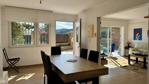 A spacious dining area with a wooden table and chairs, large windows, and a view of a garden and mountains. - Apartment with private pool only 400 mts from the beach . Very close Sa Riera. (Sa Riera)