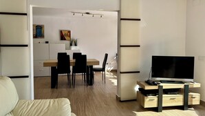 A modern living room with a sofa, a TV stand, and a dining area with a table and chairs. - Apartment with private pool only 400 mts from the beach . Very close Sa Riera. (Sa Riera)