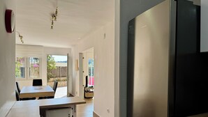 A modern kitchen with a stainless steel refrigerator, a dining area with a table and chairs, and a view of the outside through a glass door. - Apartment with private pool only 400 mts from the beach . Very close Sa Riera. (Sa Riera)