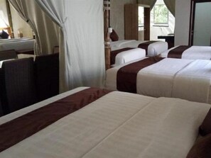A hotel room with four beds arranged in a row, a window with curtains, and a desk with a chair. - Maribaya Glamping Tent (Lembang)