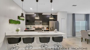 A modern kitchen with dark cabinets, a white countertop, and three black bar stools.
