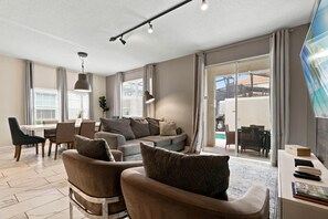 A modern living room with a sofa, armchairs, a dining table, and a TV.