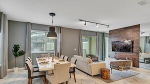 A modern living room with a dining area, a sofa, a coffee table, and a TV mounted on a wooden wall.