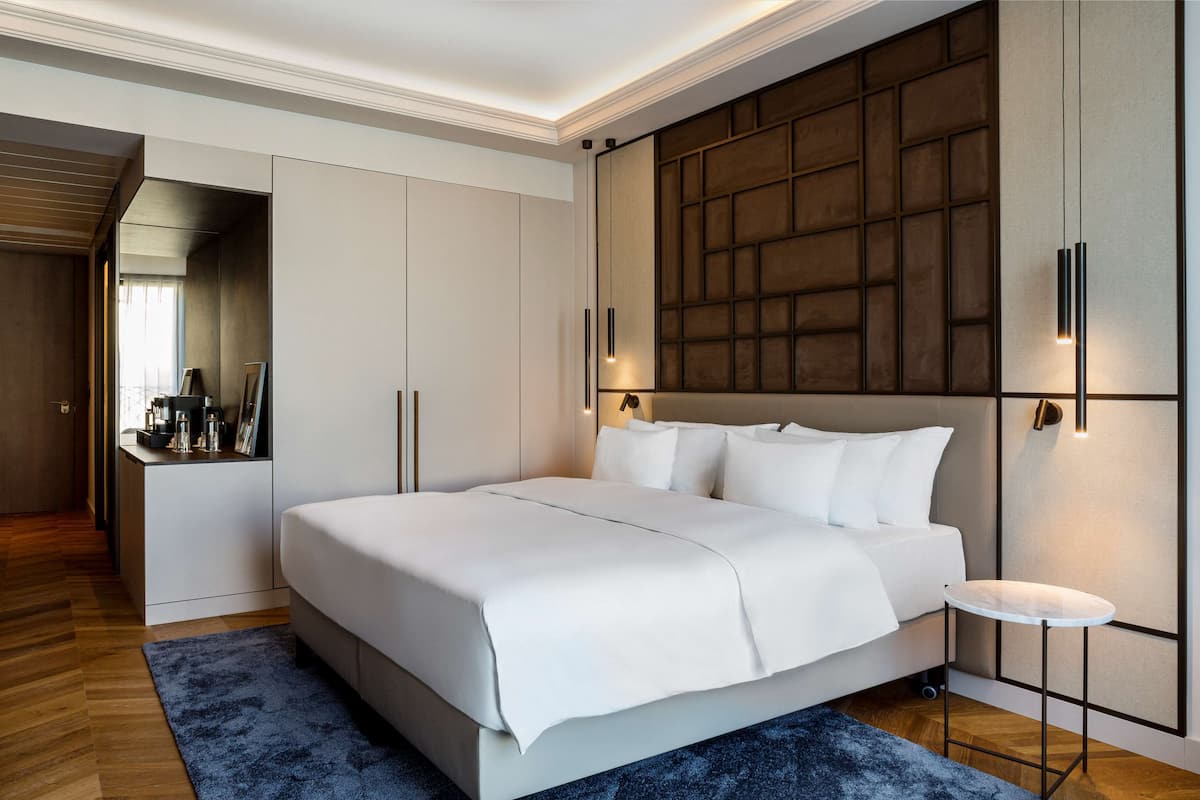 A modern bedroom with a large bed, a small table, and a wardrobe.