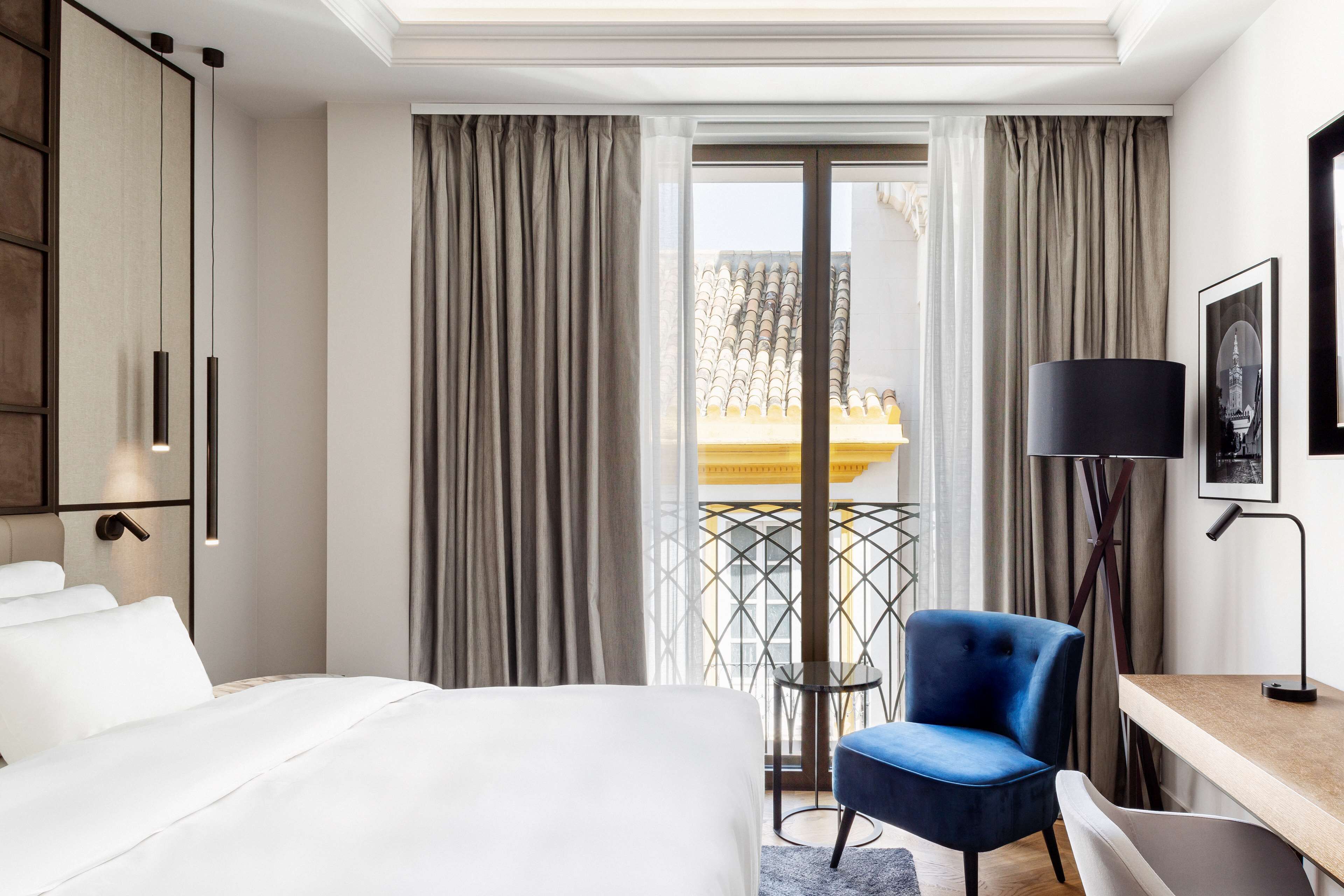 Hotellihuone, jossa on sänky, työpöytä, tuoli, lamppu ja ikkunasta avautuva näkymä ulos.