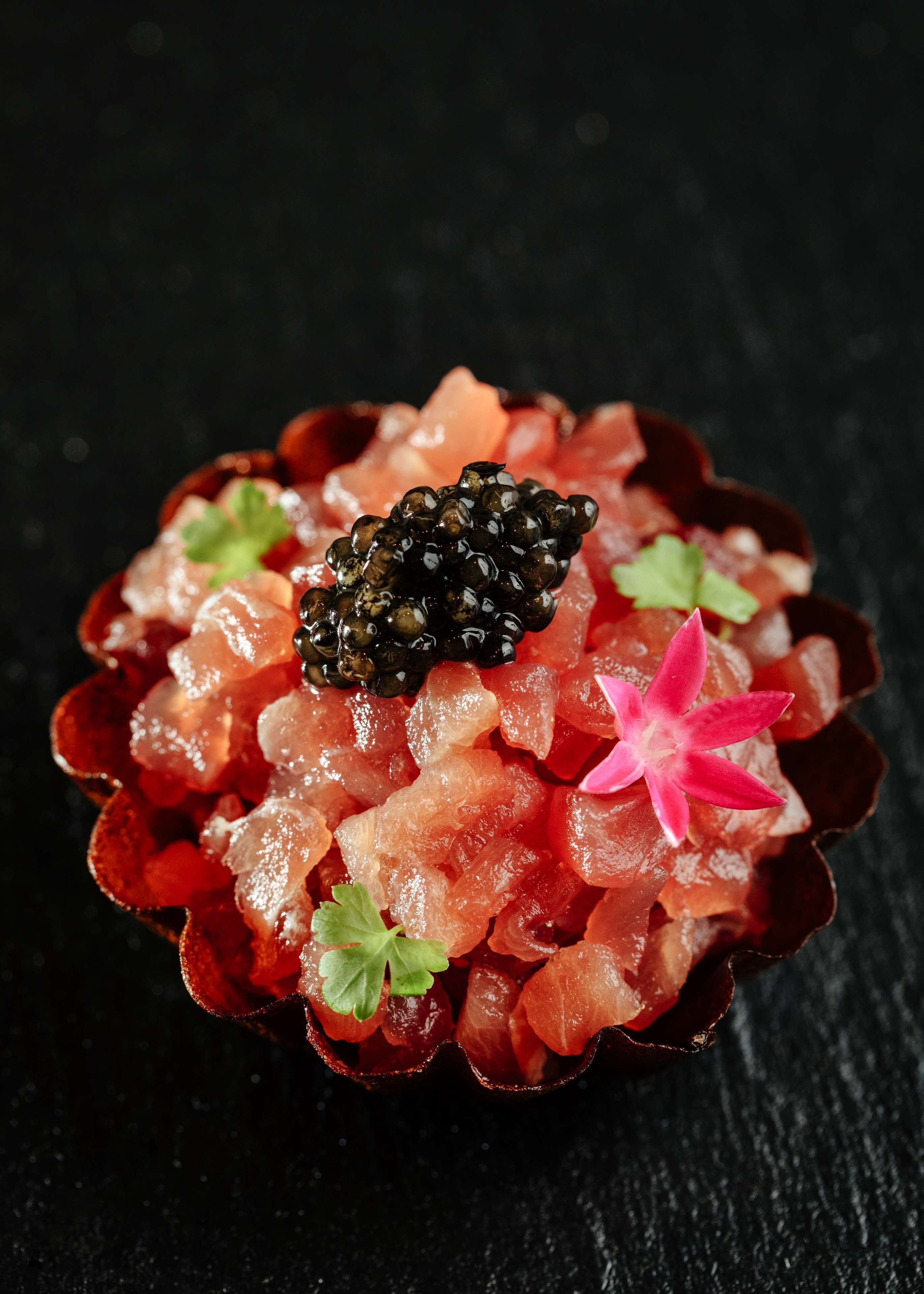 A dessert with caviar and a pink flower on top.