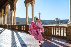 A person in a pink dress dancing in an open plaza with historical architecture in the background.